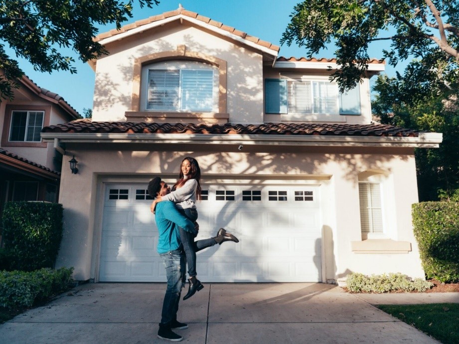 A man and woman are outside in front of their house.