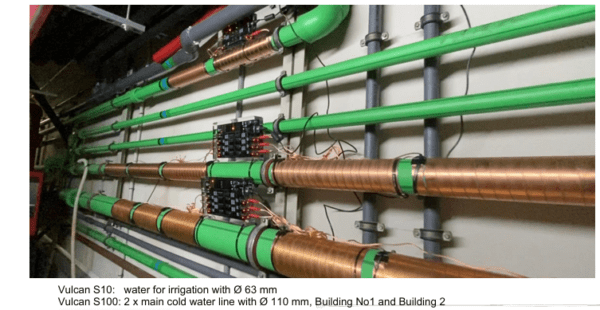 A wall of pipes with green piping and copper tubes.